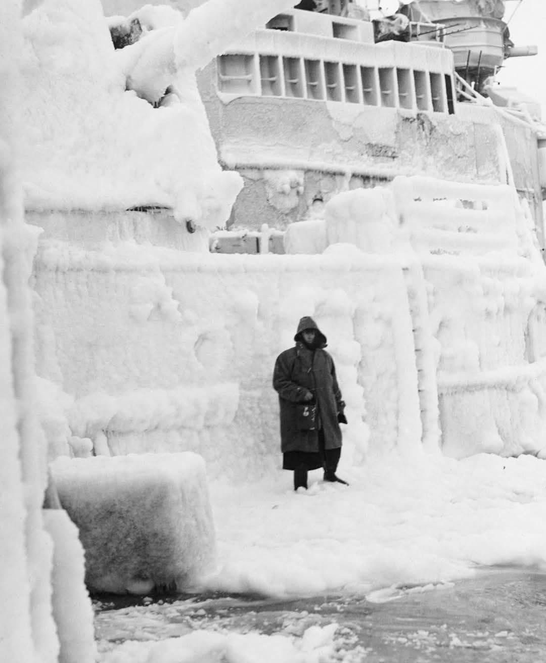 A Royal Navy sailor stands guard by the icy turrets of the HMS Belfast, escorting a convoy to the Soviet Union in 1943.