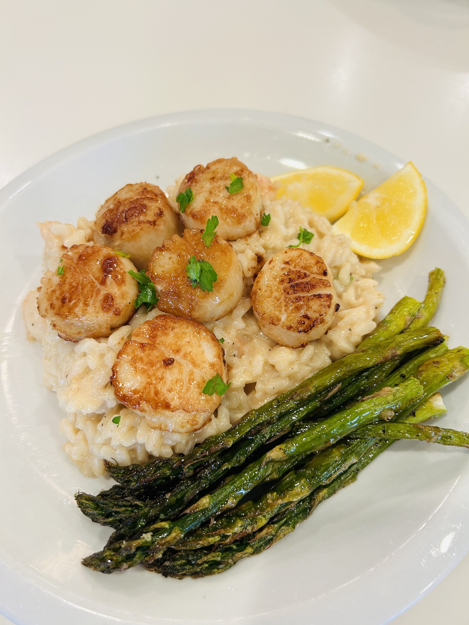 Delicious seared scallops served on a bed of shrimp risotto with roasted asparagus