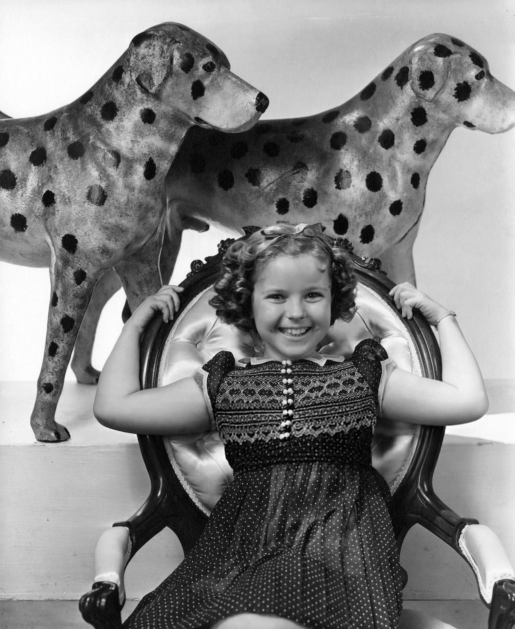 A nostalgic glimpse of Shirley Temple in 1938, elegantly seated with her Dalmatian companions.