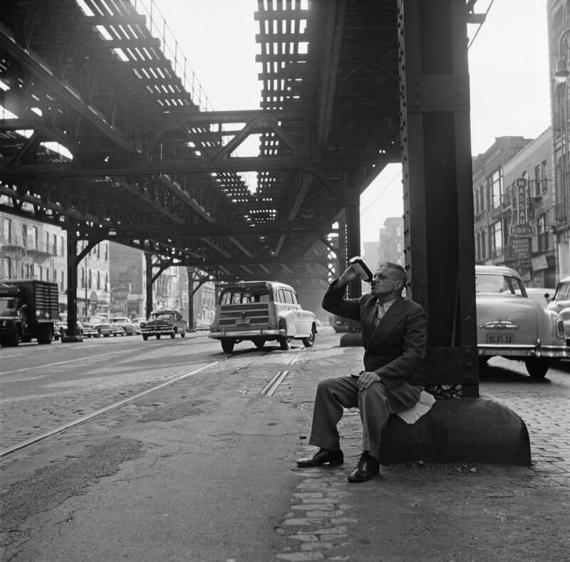 A man enjoying a drink beneath the El train on the Bowery in NYC, 1955